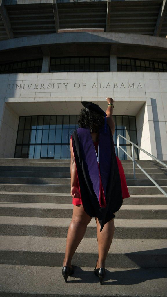 A graduate in gown and cap celebrates outside the University of Alabama.