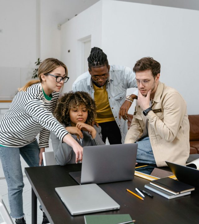 Diverse group of coworkers collaborating on a project using a laptop in a modern office.